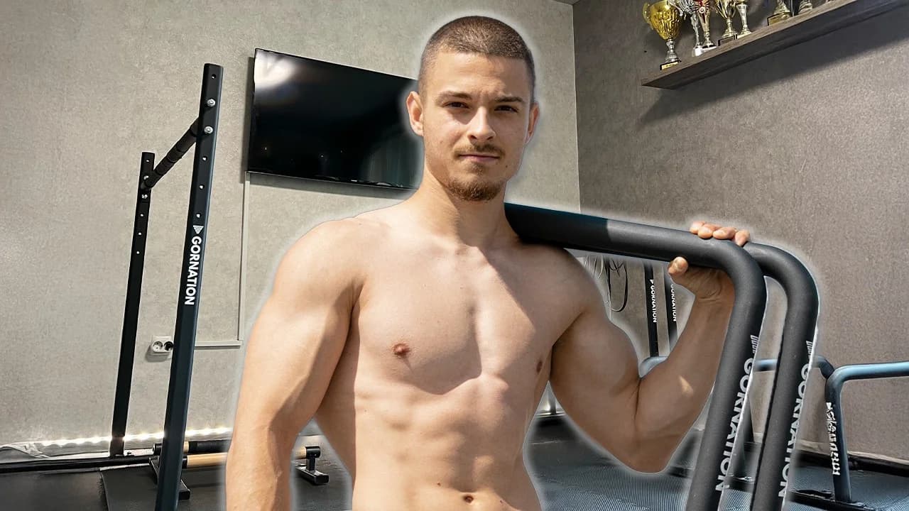 Daniel Hristov standing in his home calisthenics gym with GORNATION parallettes, dip bars, and a mounted pull-up bar