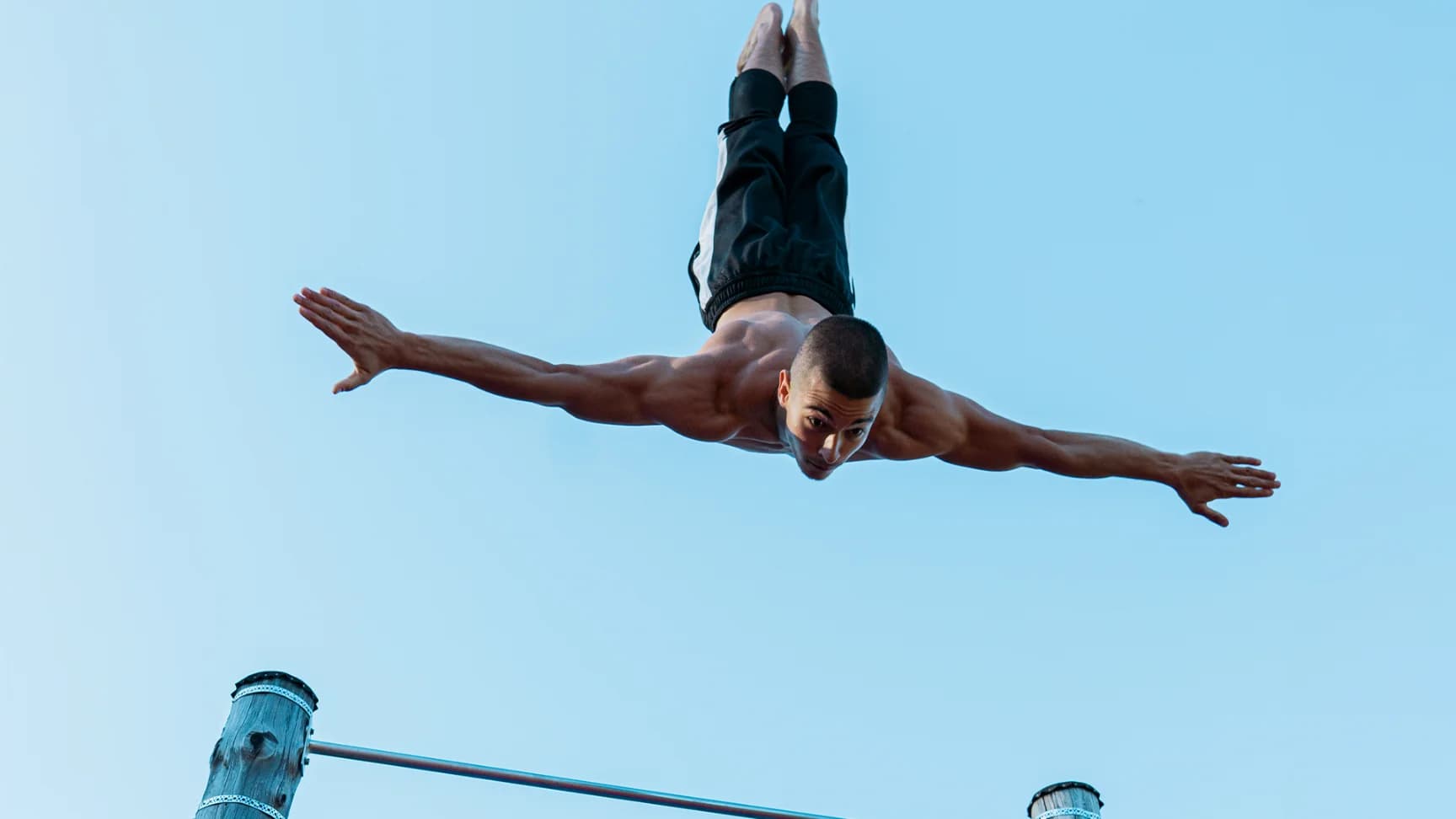 Daniel Hristov flying spread-eagle above a pull-up bar during an outdoor freestyle trick