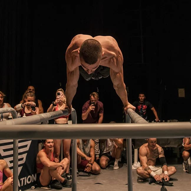 Daniel Hristov holding a planche on parallel bars in front of a competition crowd