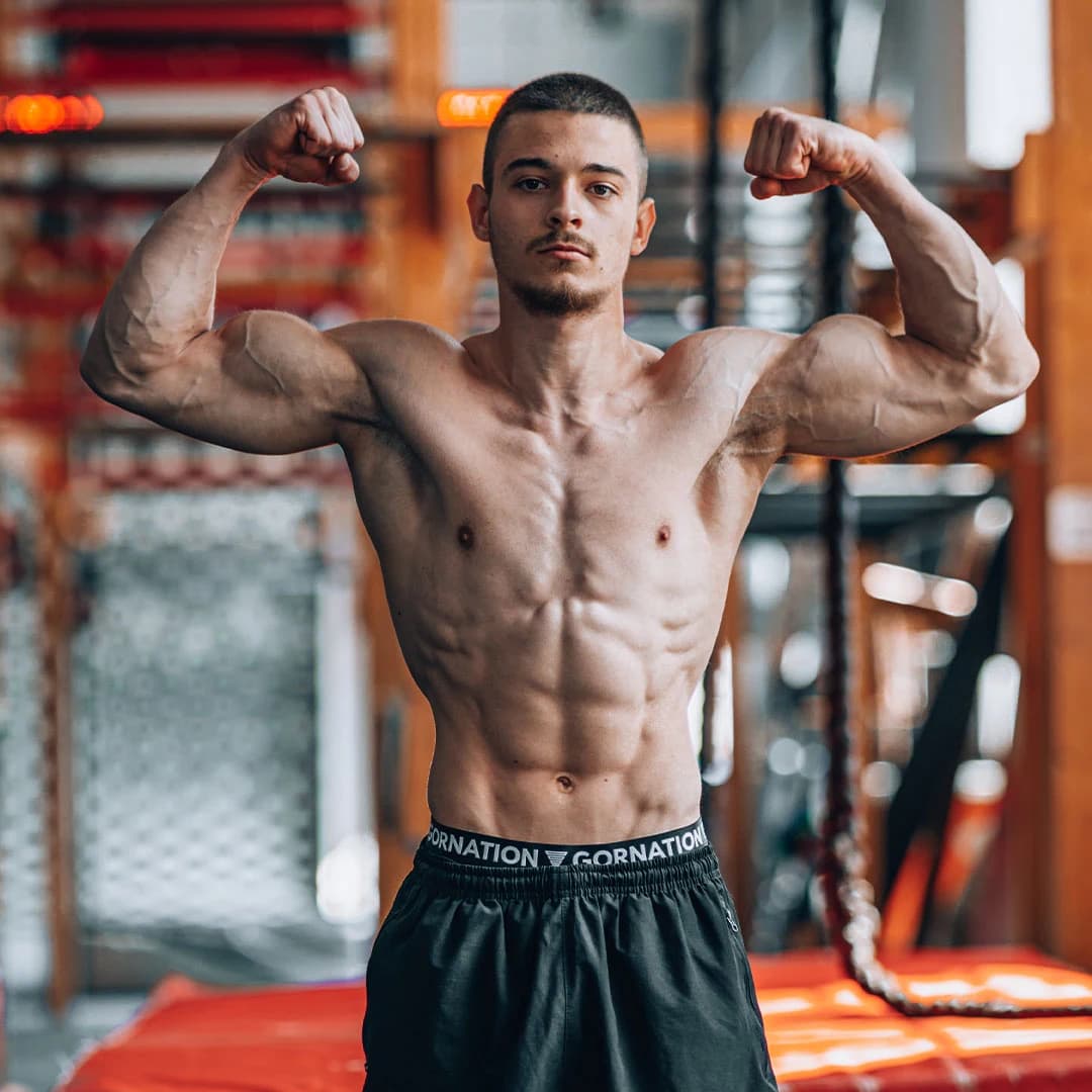 Daniel Hristov flexing both arms in a calisthenics gym