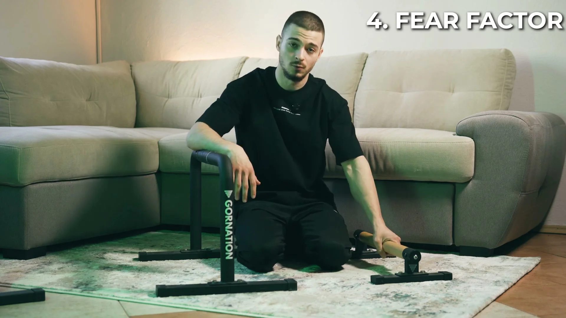 Daniel Hristov kneeling with one hand on the low metal parallette base, talking about the fear factor of training on taller equipment