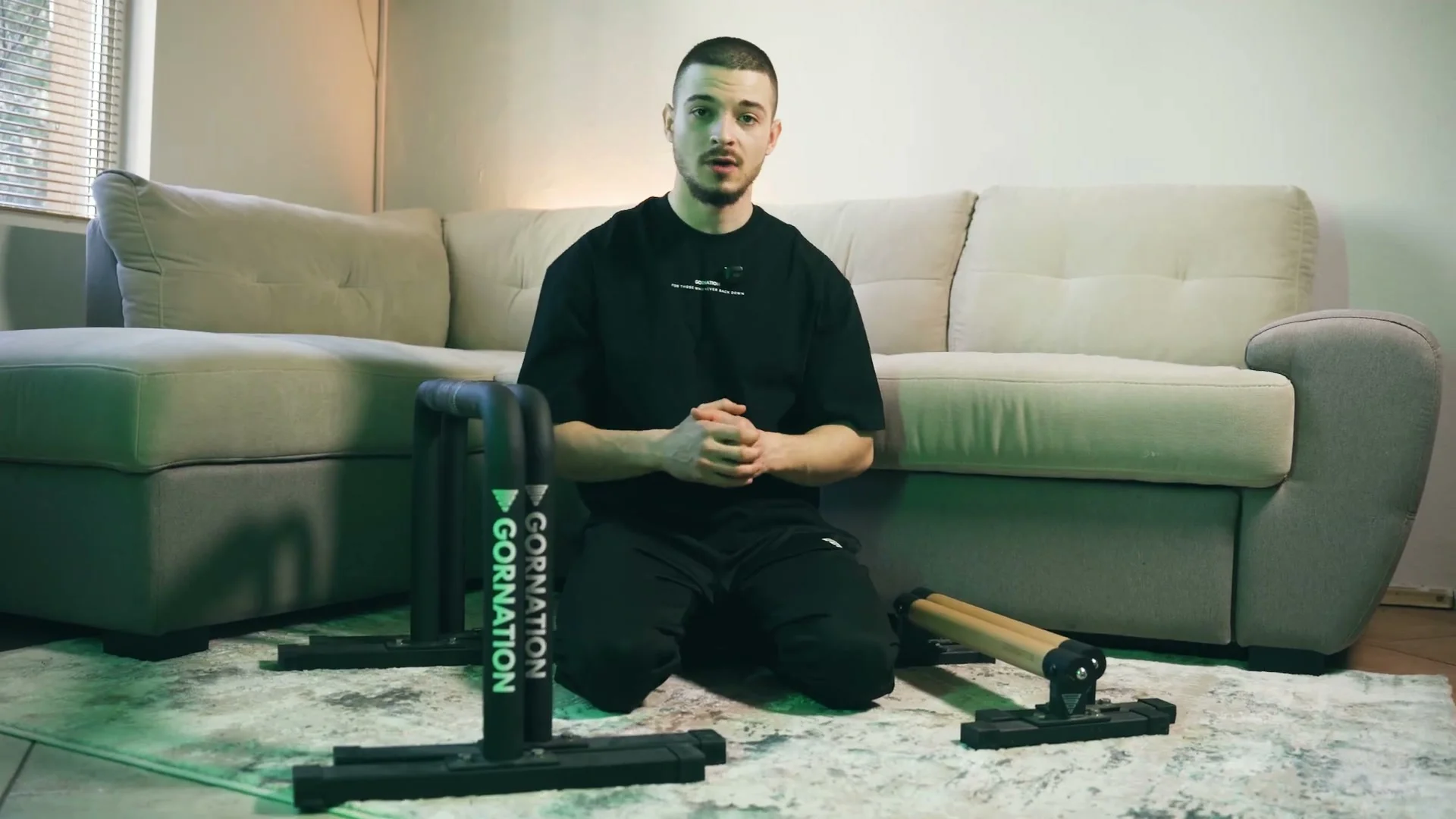 Daniel Hristov sitting between a wooden parallette pair and a metal parallette pair on his couch, comparing both sets
