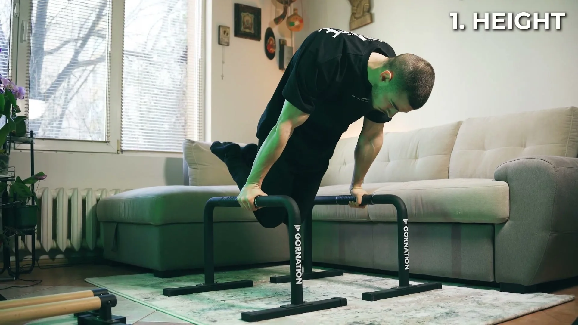 Daniel Hristov demonstrating a deep tuck planche lean on the tall metal parallettes with his knees hovering above the floor
