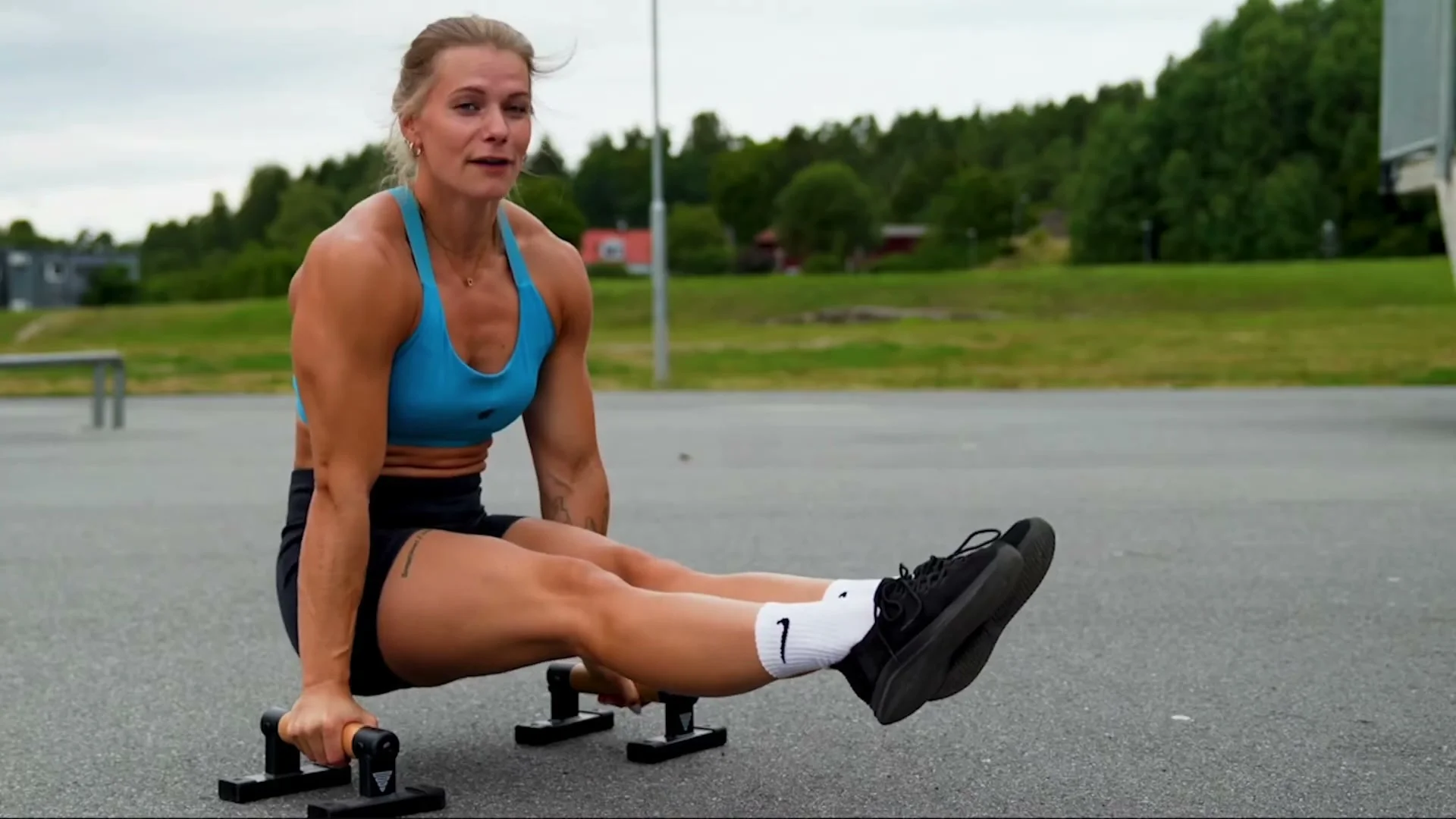 An athlete holding an L-sit on parallettes outdoors with legs extended straight in front